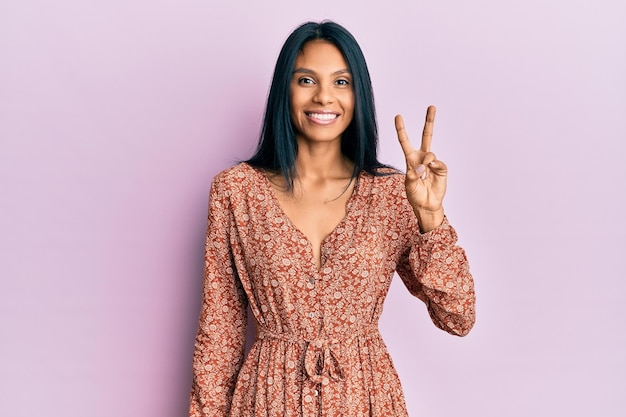 Young african american woman wearing summer dress smiling with happy face winking at the camera doing victory sign number two