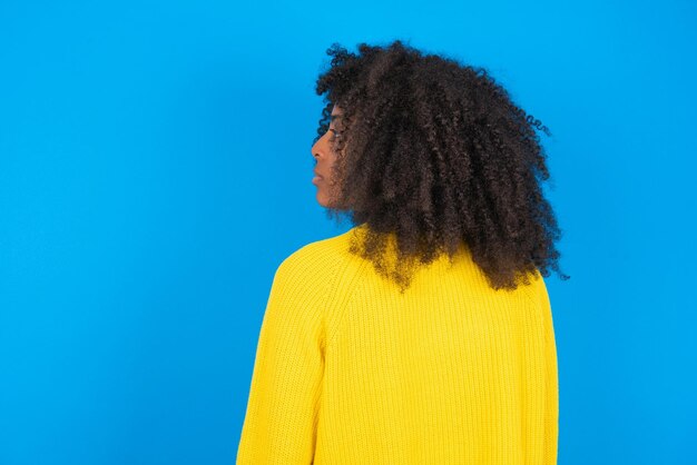Young African American woman wearing yellow sweater standing over blue background