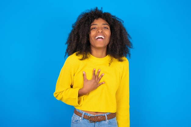 Young African American woman wearing yellow sweater standing over blue background