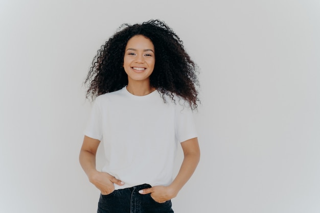 Young African American woman wears white t shirt, expresses good emotions