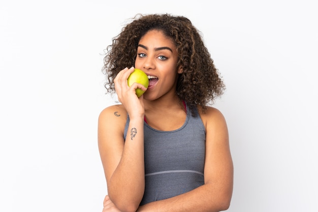 Young African American woman on white wall eating an apple