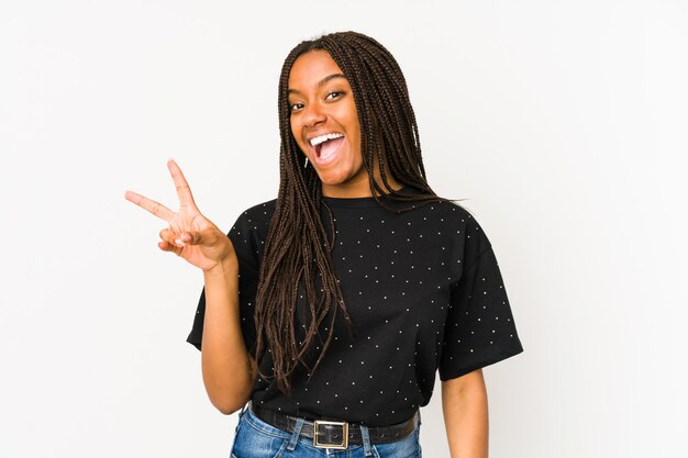 Young african american woman on white wall joyful and carefree showing a peace symbol with fingers.