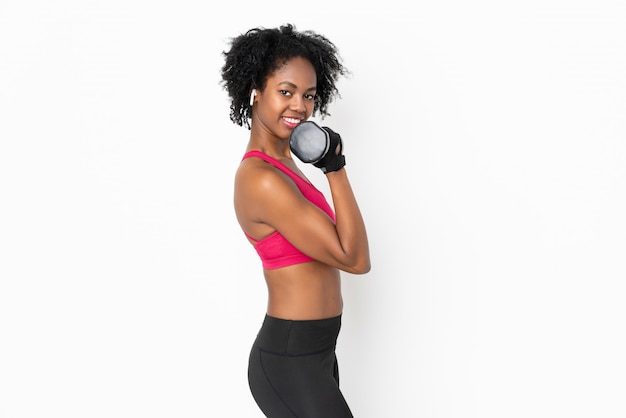 Young African American woman on white wall making weightlifting