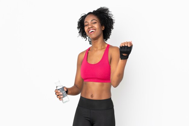 Young African American woman on white wall with sports water bottle