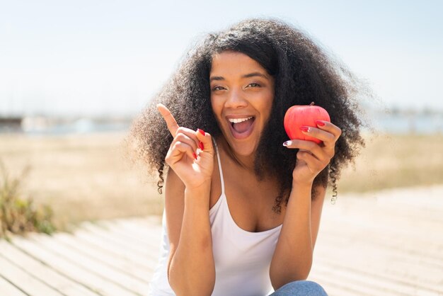 Young African American woman with an apple at outdoors pointing up a great idea