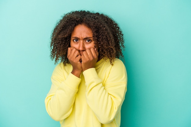 Photo young african american woman with curly hair isolated on blue background biting fingernails, nervous and very anxious.
