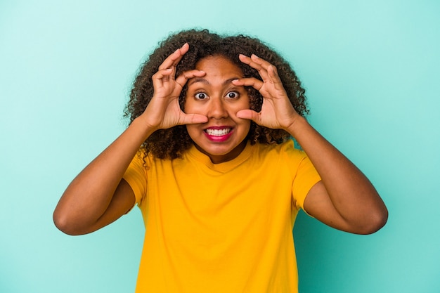 Young african american woman with curly hair isolated on blue background keeping eyes opened to find a success opportunity.