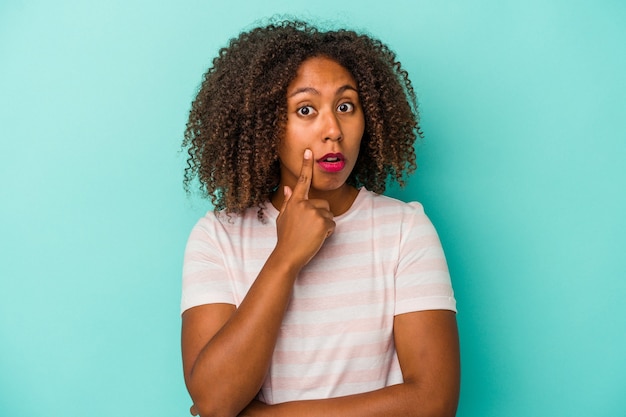 Young african american woman with curly hair isolated on blue background looking sideways with doubtful and skeptical expression.