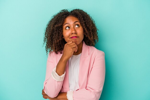 Young african american woman with curly hair isolated on blue background relaxed thinking about something looking at a copy space.