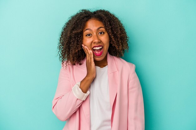 Young african american woman with curly hair isolated on blue background shouts loud, keeps eyes opened and hands tense.