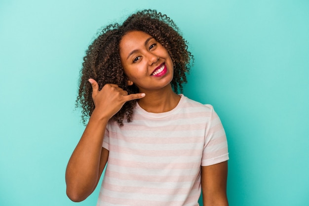 Young african american woman with curly hair isolated on blue background showing a mobile phone call gesture with fingers.