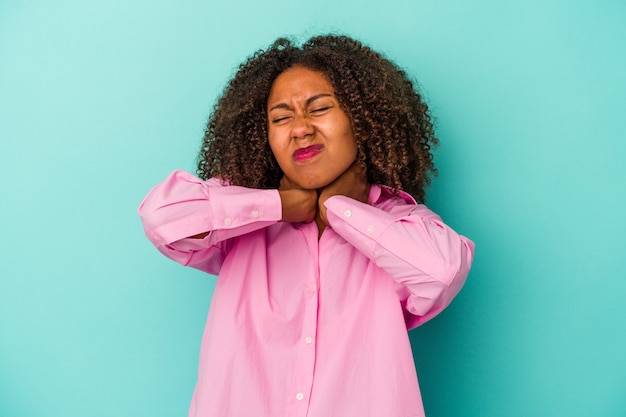 Young african american woman with curly hair isolated on blue background suffering neck pain due to sedentary lifestyle.