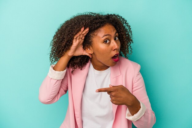 Young african american woman with curly hair isolated on blue background trying to listening a gossip.