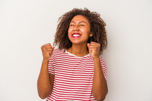 Foto giovane donna afroamericana con capelli ricci isolati su fondo bianco che celebra una vittoria, passione ed entusiasmo, espressione felice.