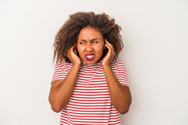 Young african american woman with curly hair isolated on white background covering ears with hands.