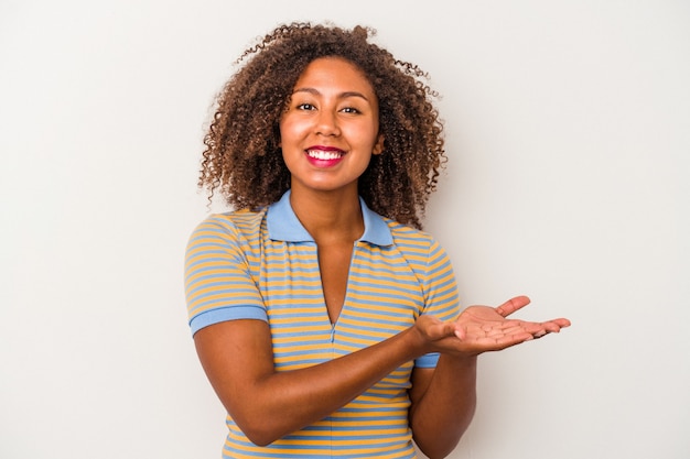 Young african american woman with curly hair isolated on white background holding a copy space on a palm.