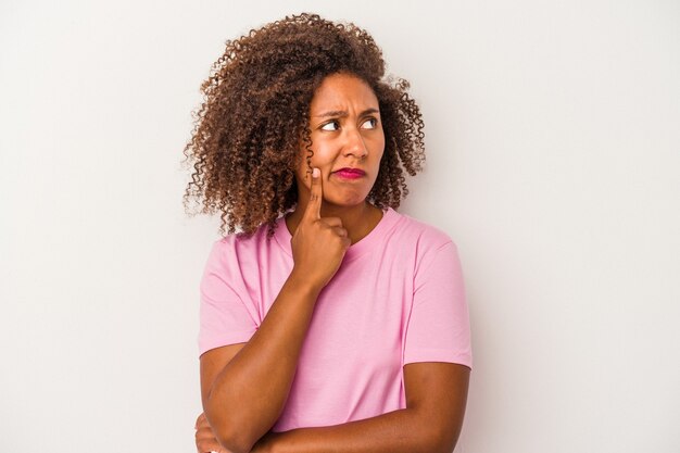 Giovane donna afroamericana con capelli ricci isolati su fondo bianco che guarda obliquamente con espressione dubbiosa e scettica.