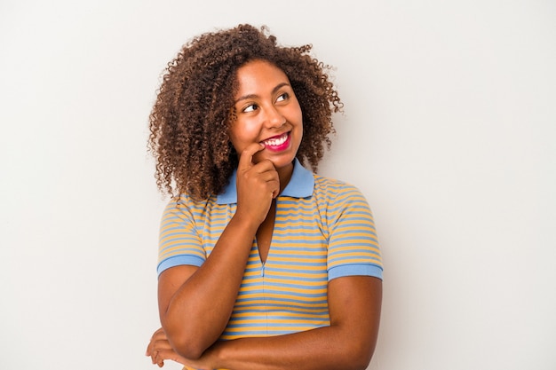 곱슬머리를 흰색 배경에 격리한 젊은 아프리카계 미국인 여성은 복사 공간을 보고 있는 무언가에 대해 편안하게 생각했습니다.