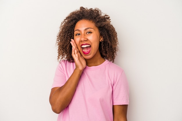 Young african american woman with curly hair isolated on white background shouts loud, keeps eyes opened and hands tense.