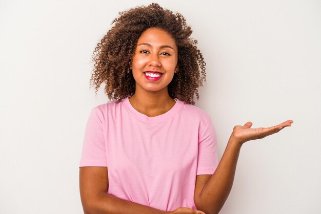 Young african american woman with curly hair isolated on white background showing a copy space on a palm and holding another hand on waist