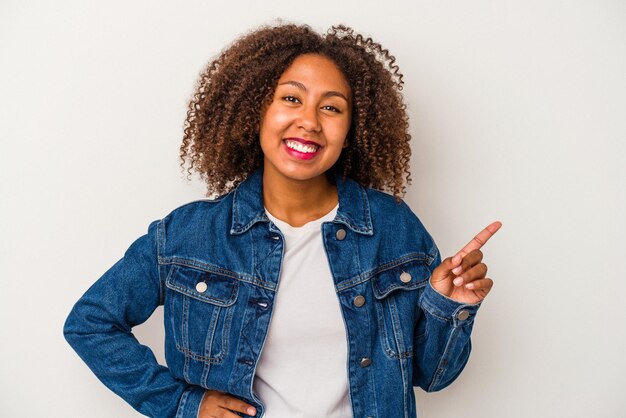 Young african american woman with curly hair isolated on white background smiling cheerfully pointing with forefinger away