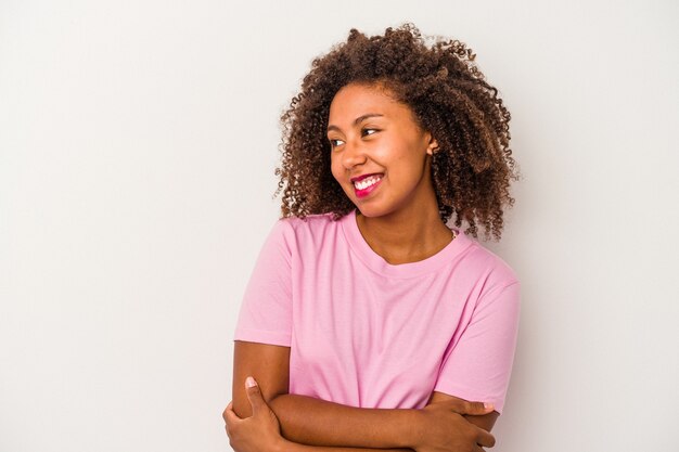 Giovane donna afroamericana con capelli ricci isolati su fondo bianco sorridente fiducioso con le braccia incrociate.