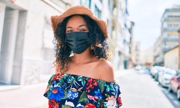 Young african american woman with curly hair wearing coronavirus safety mask outdoors