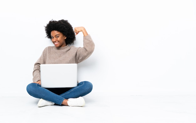 Young African American woman with a laptop sitting on the floor doing strong gesture