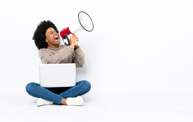 Young African American woman with a laptop sitting on the floor shouting through a megaphone