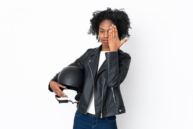 手で目を覆っている白い壁にオートバイのヘルメットを持つ若いアフリカ系アメリカ人女性