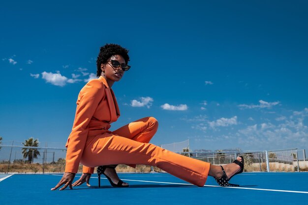 Young African American woman with short hair and sunglasses dressed in a stylish orange outfit