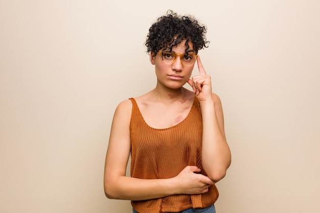 Young african american woman with skin birth mark pointing temple with finger, thinking, focused on a task.