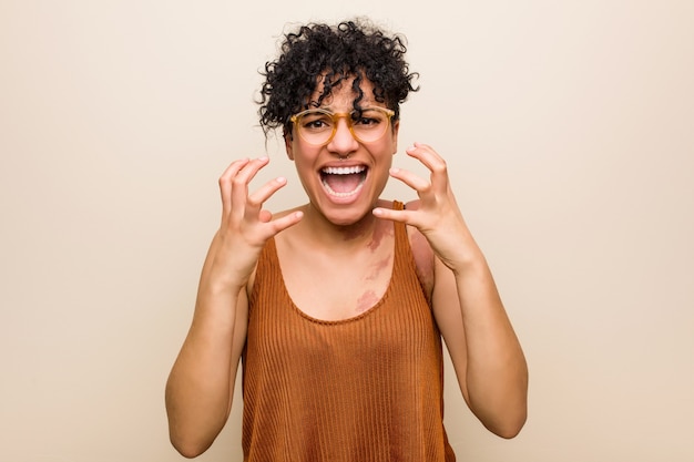 Young african american woman with skin birth mark upset screaming with tense hands.