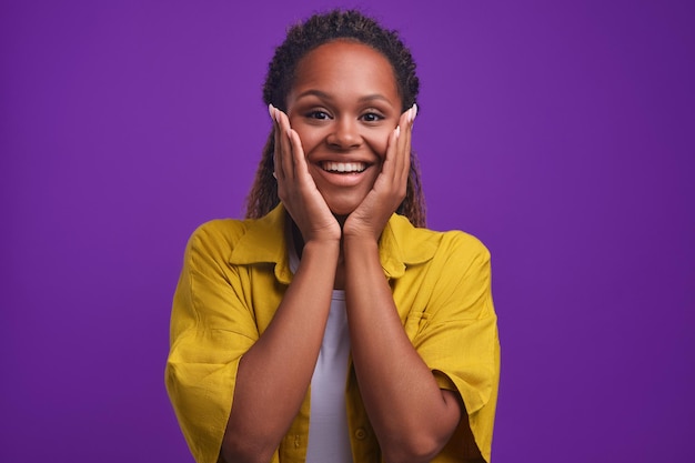 Young african american woman with smiling hands to cheeks stands in studio