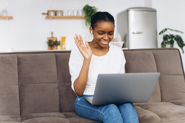 Young African American woman working on laptop sitting on sofa in kitchen