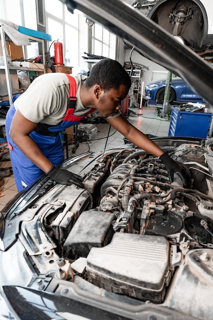 若いアフリカの自動車メカニックが自動車サービスで車のエンジンをハッドの下でチェックしています