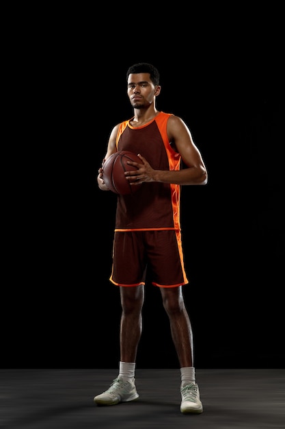 Young african basketball player training on black studio background.