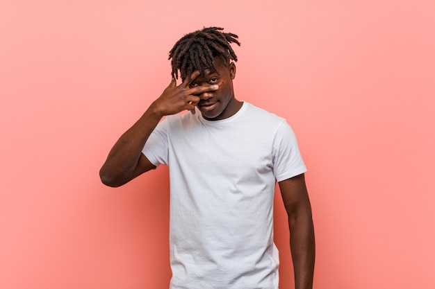 Young african black man blink at through fingers, embarrassed covering face.