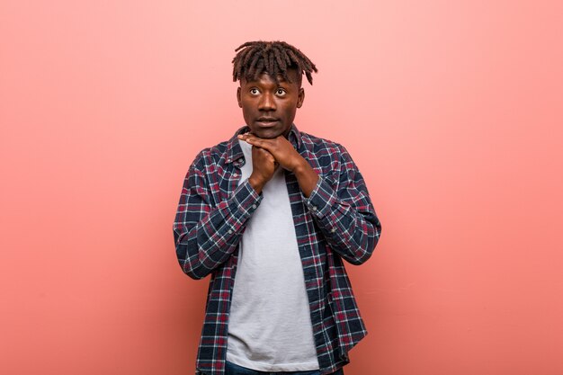 Young african black man keeps hands under chin, is looking happily aside.