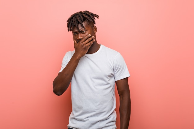 Young african black man thoughtful looking to a copy space covering mouth with hand.