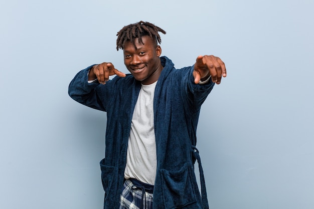 Young african black man wearing pajama cheerful smiles pointing to front.