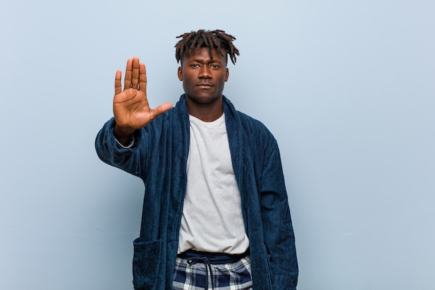 Young african black man wearing pajama standing with outstretched hand showing stop sign, preventing you.