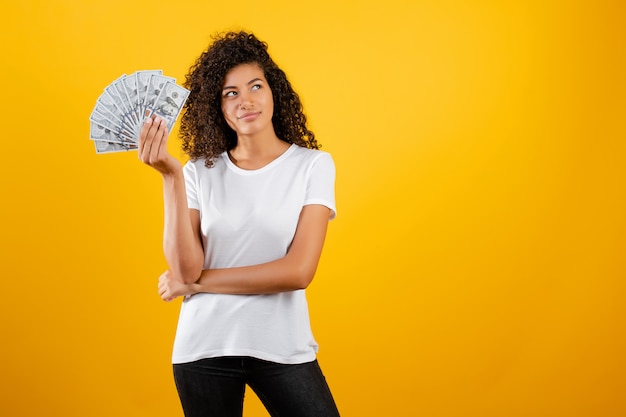 Молодая африканская чернокожая женщина с деньгами долларов в руке изолированная над желтым цветом