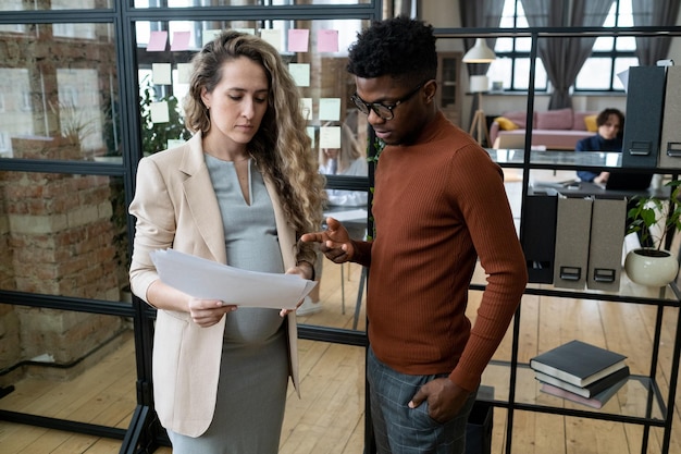 Photo young african businessman and his pregnant colleague discussing papers