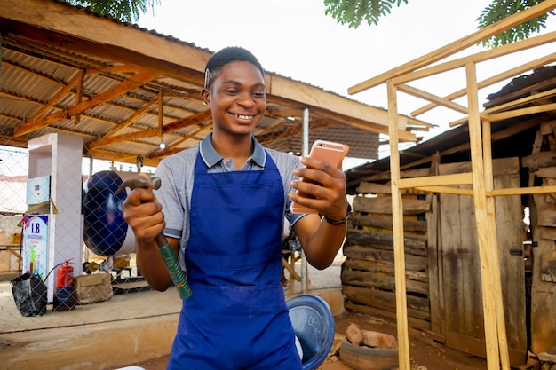 Photo young african carpenter standing holding working phone