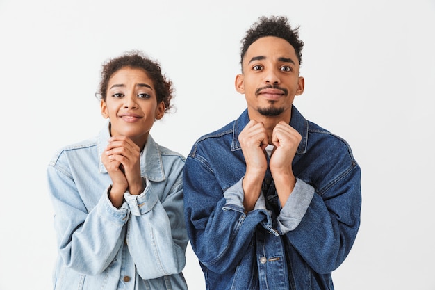 Photo young african couple in denim shirts praying together with arms near face  over grey wall