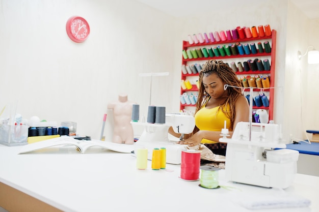 Young african dressmaker woman sews clothes on sewing machine at tailor office Black seamstress women