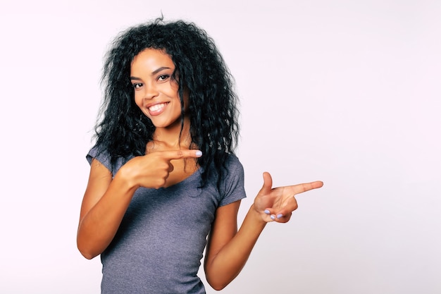 Young African ethnic woman with medium-length black hair is looking at the camera and pointing with finger guns