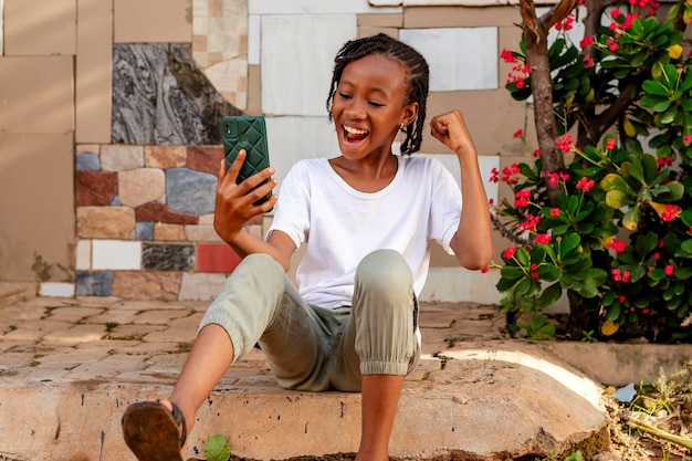 Молодая африканская девушка, наполненная волнением, погружена в использование своего мобильного телефона.