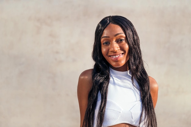 Young african girl smiling happy with a gray concrete wall in the background, concept of youth and racial diversity, copy space for text